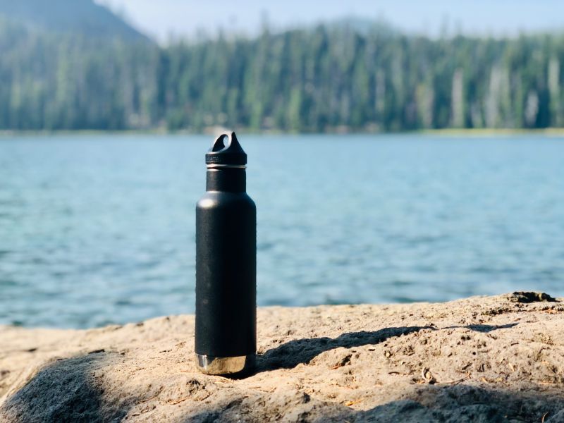 black water bottle on a rock beside river and forest ahead