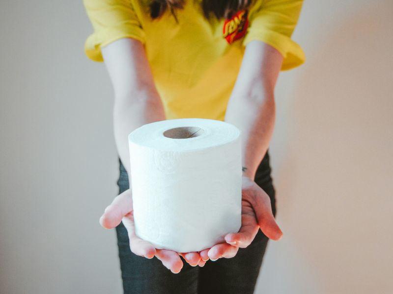 toilet paper in hand of a women with yellow top